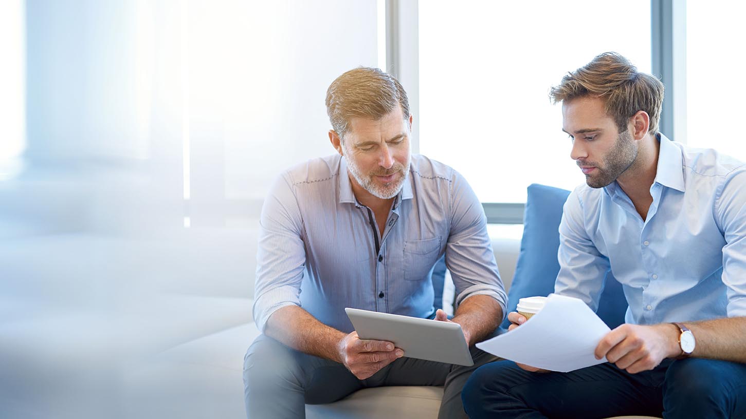 Mature businessman using a digital tablet to discuss information with a younger colleague in a modern business lounge