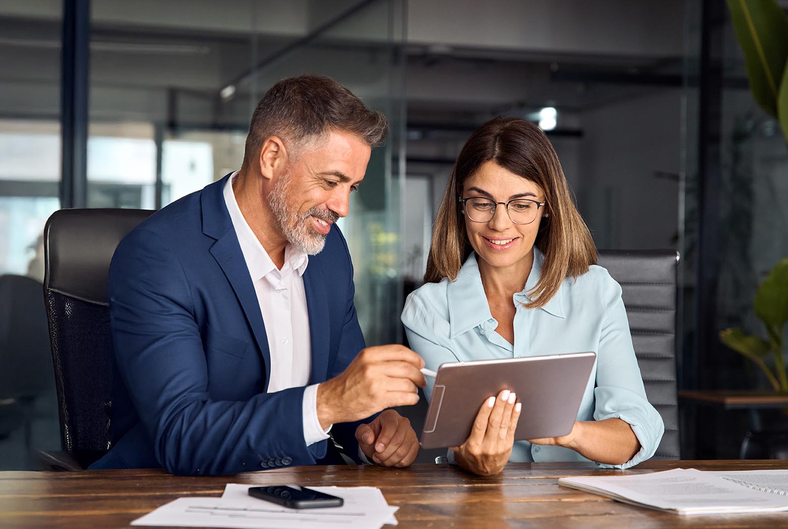 Two colleagues, group of partners, professional people working together. Mature 50s age Latin business man mentoring mid age European woman discussing project on tablet in office. Banner, copy space